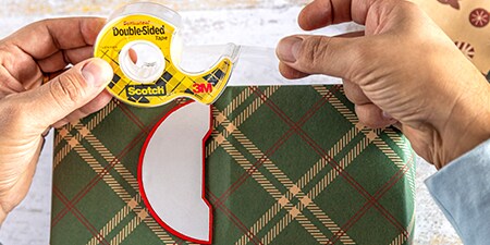 Attaccare decorazioni a un regalo impacchettato utilizzando il Nastro biadesivo Scotch®
