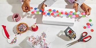 Impacchettare una scatola regalo con nastro di coriandoli realizzato attaccando coriandoli colorati al nastro adesivo Scotch®
