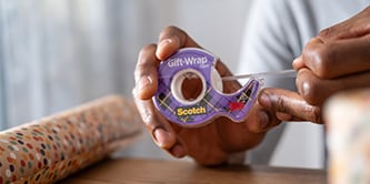 Uomo che impacchetta un regalo con il nastro Scotch® GiftWrap
