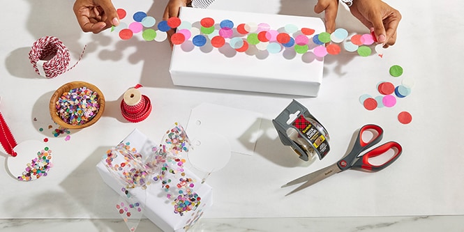 Donna e sua figlia che impacchettano una scatola regalo con nastro da imballo decorato con coriandoli colorati attaccati
