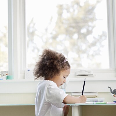 Un bambino che disegna davanti a una finestra.