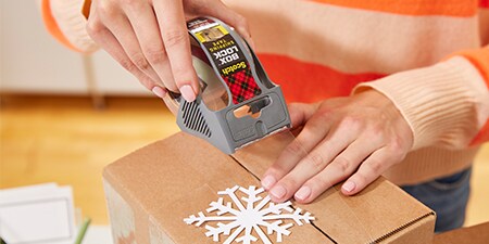 Sigillare un regalo festivo all'interno di un pacco utilizzando il Nastro adesivo Box Lock™ Scotch®
