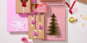 Decorazioni natalizie e lavori di carta come alberi e palline attaccati a regali impacchettati utilizzando il Nastro biadesivo Scotch®
