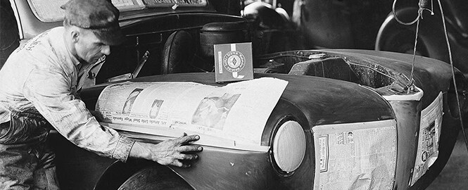 Immagine in bianco e nero che mostra un uomo che usa nastro adesivo per non danneggiare la vernice esistente durante la verniciatura della carrozzeria
